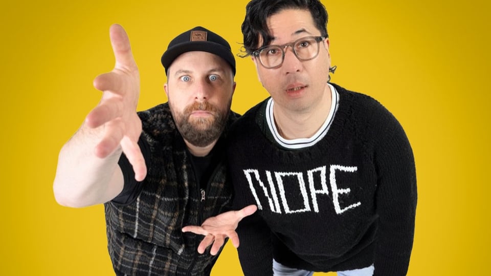 Zwei Darsteller aus CHOIR! CHOIR! CHOIR! vor gelbem Hintergrund, eine Person mit karohemd und Kappe macht eine Geste mit der Hand, die andere Person mit schwarzem Pulli mit Aufschrift