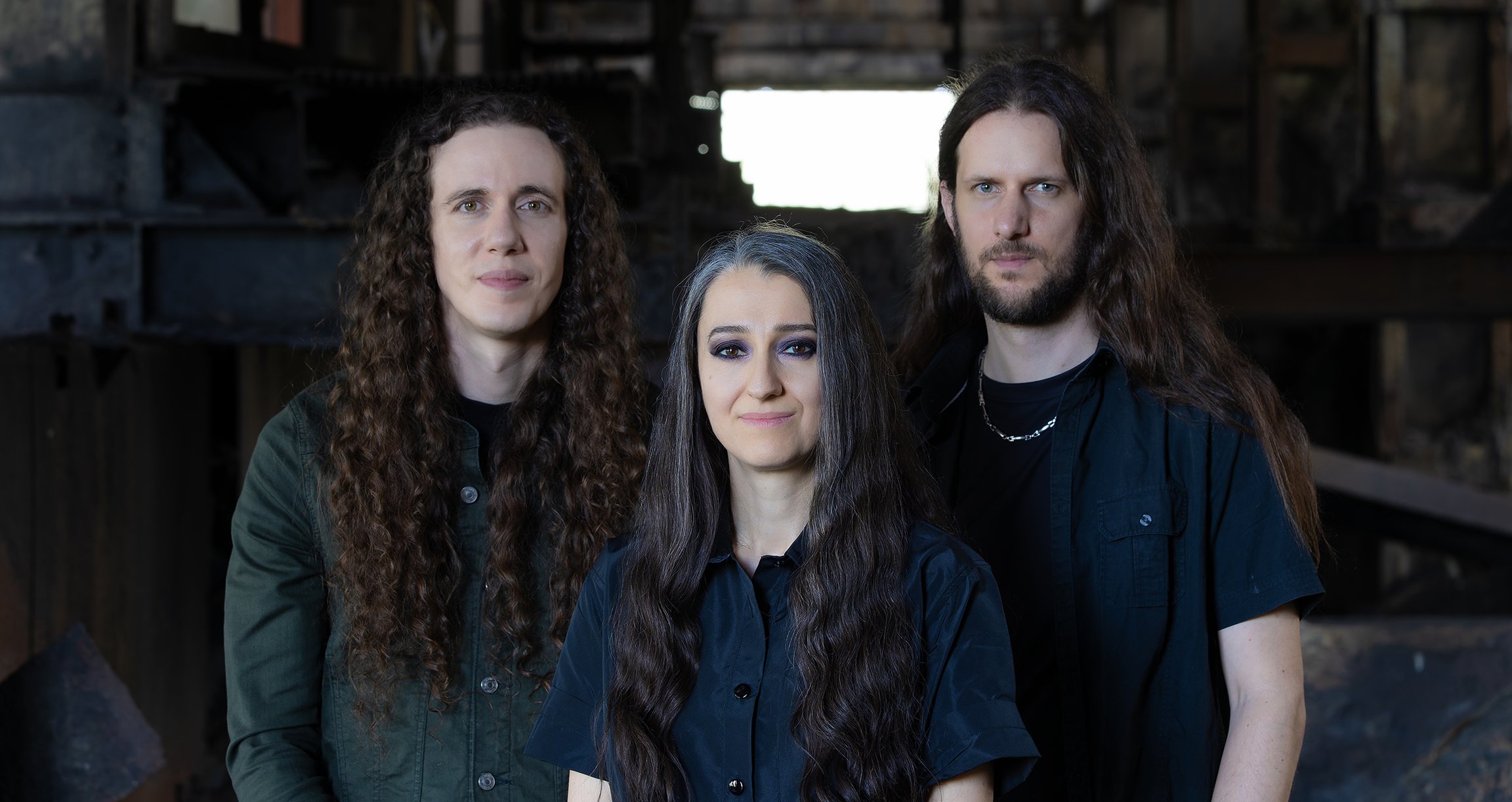 Drei Personen in dunkler Kleidung mit langen Haaren