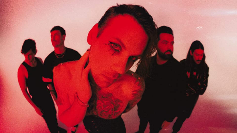 Fünfköpfige Band in rotem Licht vor hellem Hintergrund; im Vordergrund eine Person mit auffälligem Augen-Make-up und Tattoos, dahinter vier weitere Mitglieder in dunkler Kleidung – Pressefoto der Metalcore-Band Beartooth.