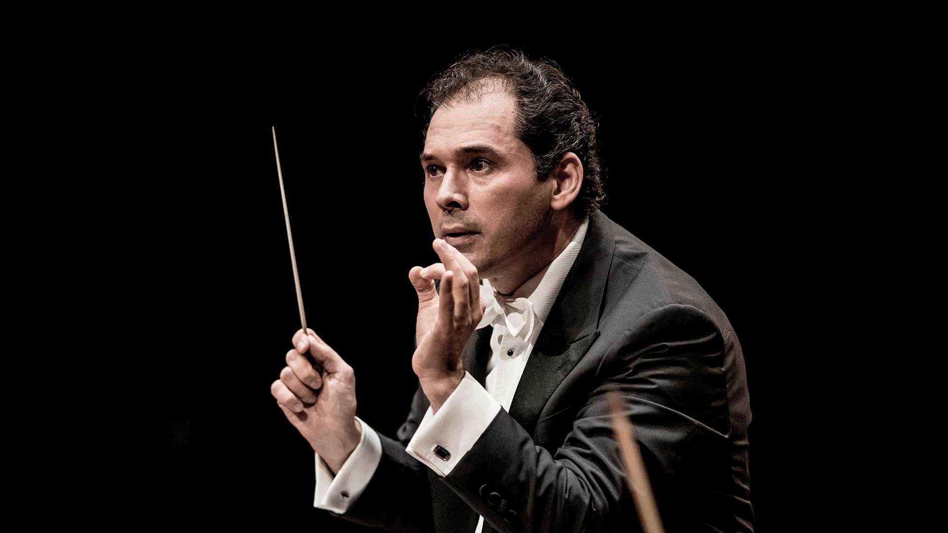 Tugan Sokhiev dirigiert und trägt dabei einen Anzug