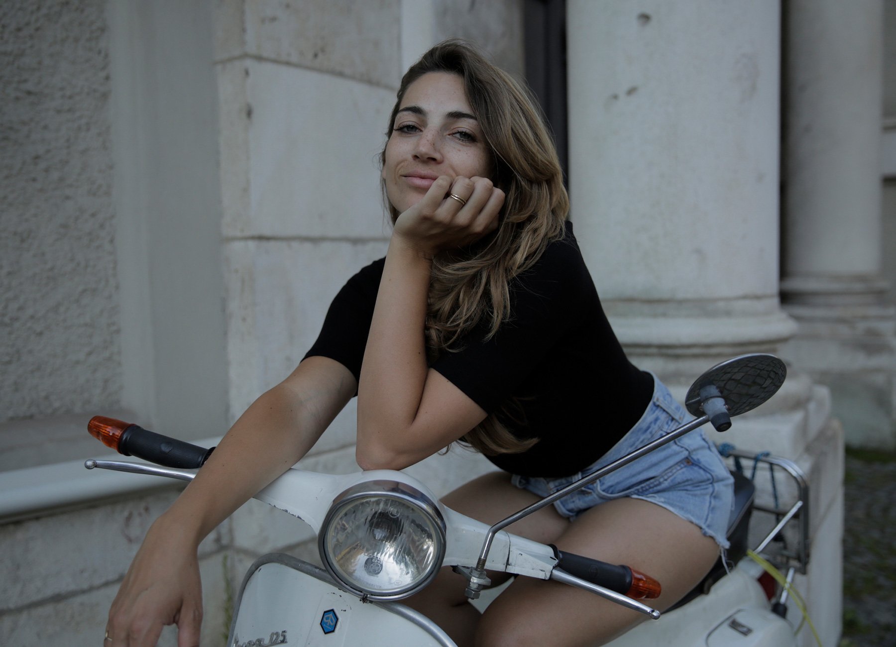 Dame mit langen Haaren schwarzem Shirt und kurzen Hosen auf weissem Motorrad