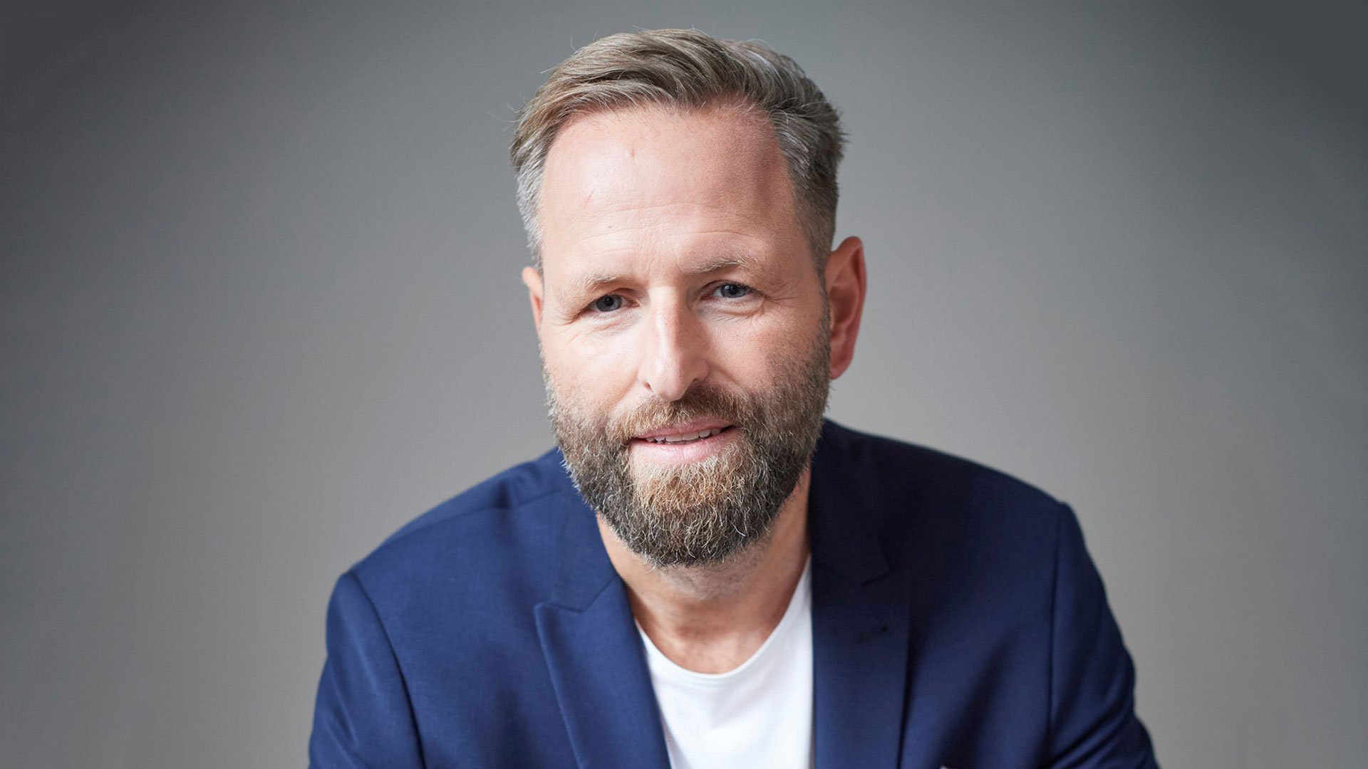 Eventfoto „Stephan Lucas“ mit dem Künstler vor grauem Hintergrund.