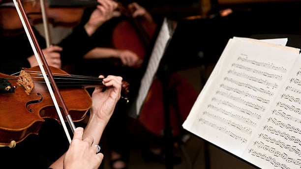 Musiker spielen Streichinstrumente, Notenblatt im Vordergrund.