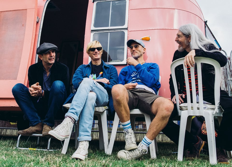 Foto der Band Kula Shaker vor einem rosa Vintage-Wohnwagen im Hintergrund