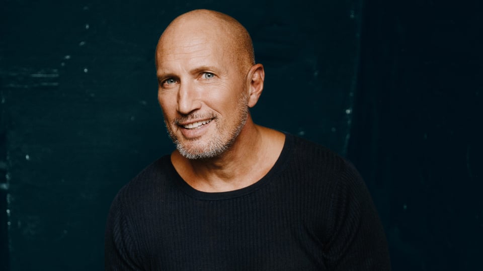 Benno Führmann lächelnd in schwarzer Kleidung vor dunklem hintergrund