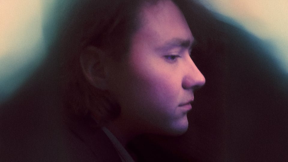 Porträt von Current Joys (Nick Rattigan) im Profil, mit weichem, farbigem Licht und unscharfem Hintergrund, stimmungsvolle Atmosphäre.