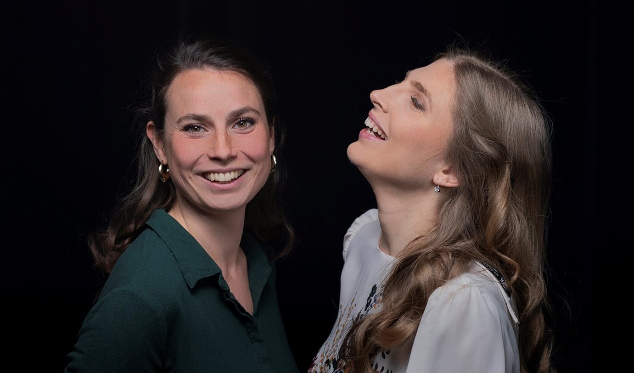 zwei Frauen lachend vor schwarzem Hintergrund