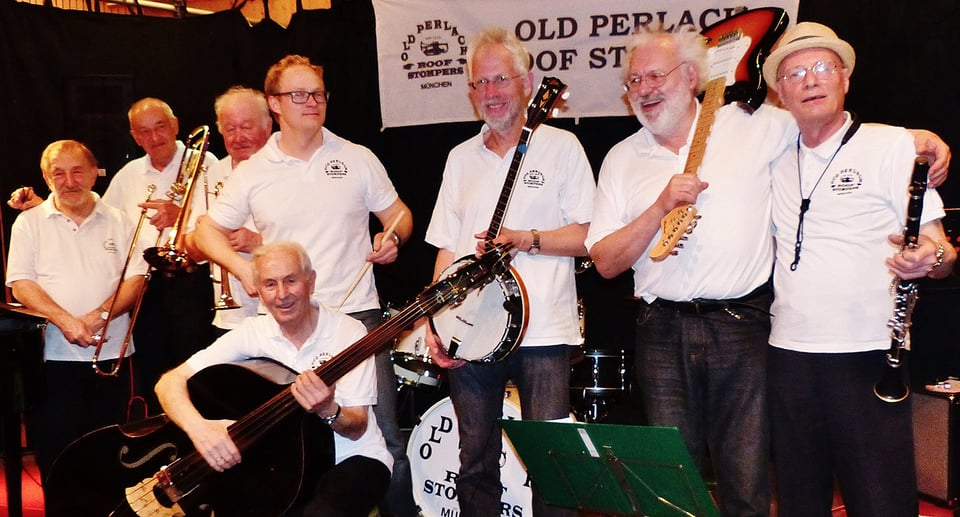 Acht Musiker in weissen Shirts und dunklen Hosen mit Instrumenten auf Bühne