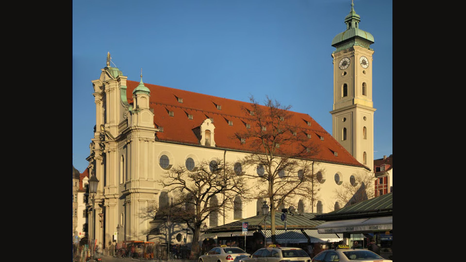 Die Heilig Geist Kirche von der Seite mit Dächsern, Autos und Bäumen im Vordergrund
