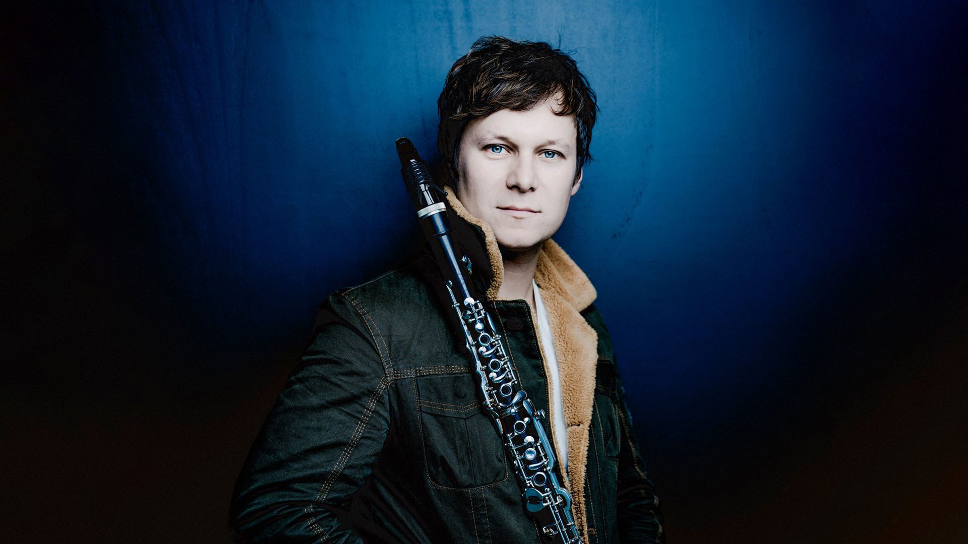 Sebastian Manz mit einem Instrument vor blau-schwarzem Hintergrund mit Farbverlauf