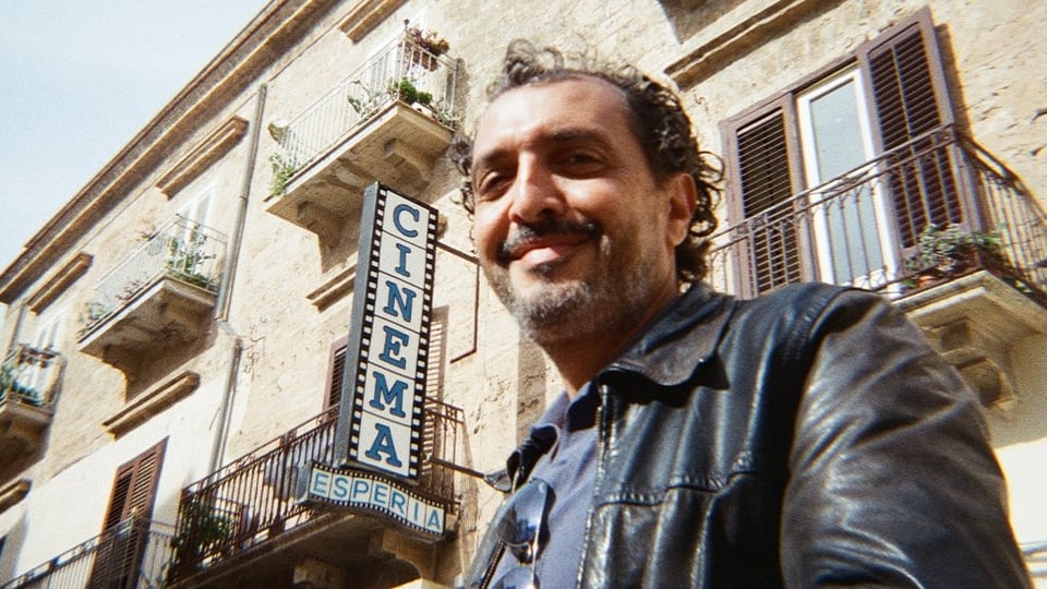 Der Künstler Kid Francescoli steht vor einer altertümlichen Hauswand mit Balkonen sowie einem Schild mit der Aufschrift Cinema