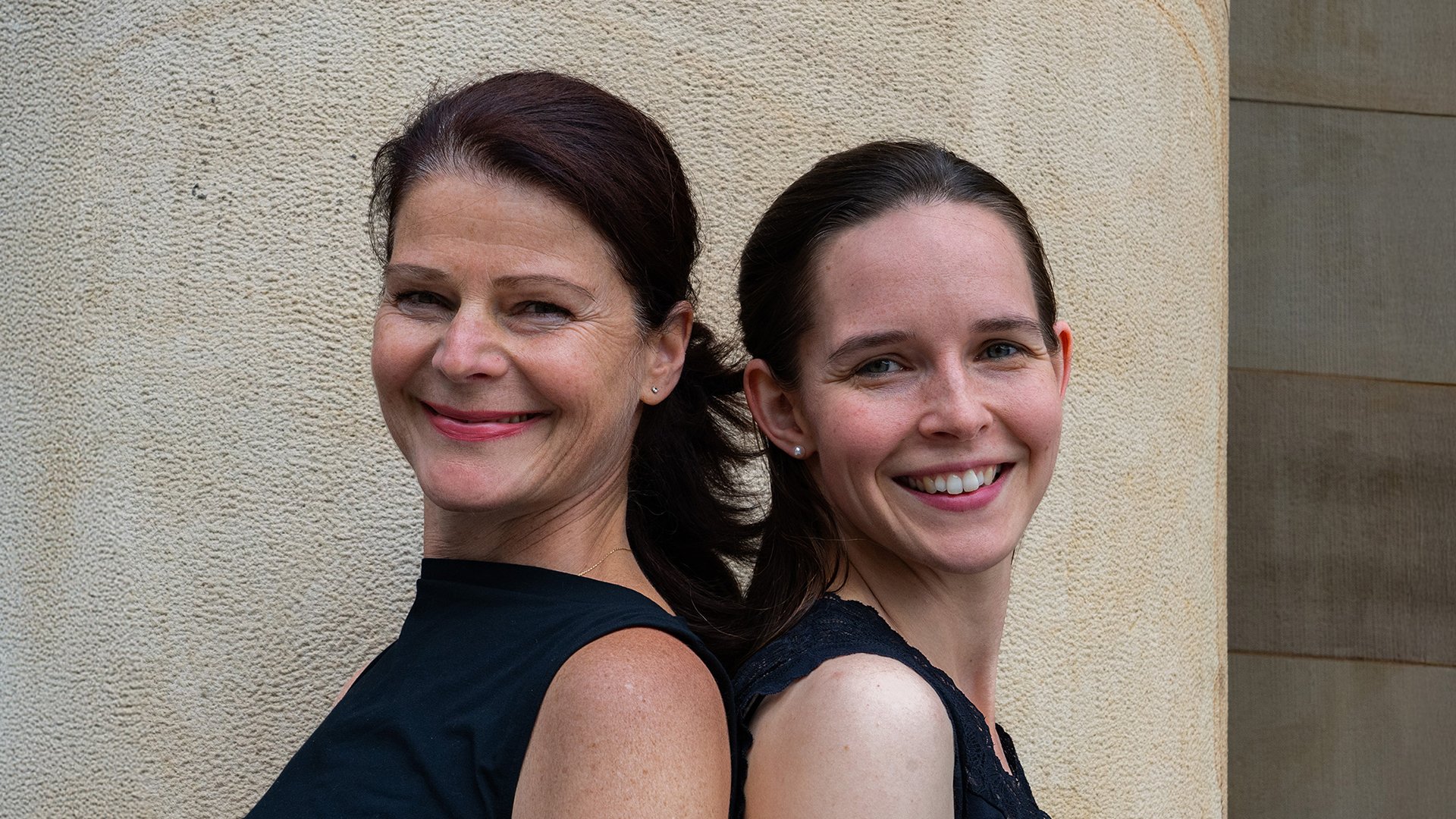 Portrait von zwei Damen in schwarzer Kleidung vor heller Mauer