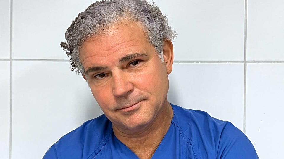 Foto von Michael Tsokos mit blauem Krankenhaushemd vor einer weißen Kachelwand wie im Krankenhaus