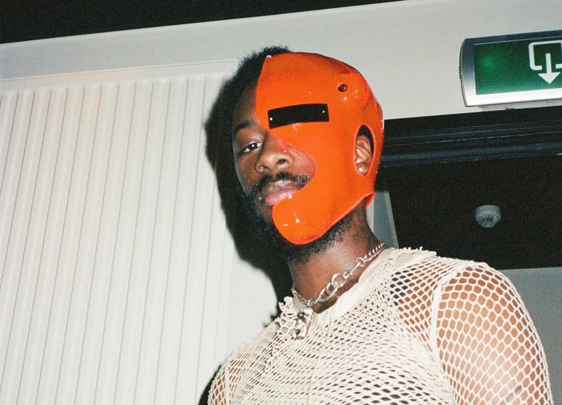 Filmfoto von Goldlink mit einer orangen Gesichtsmaske und einem weißen Netzoberteil