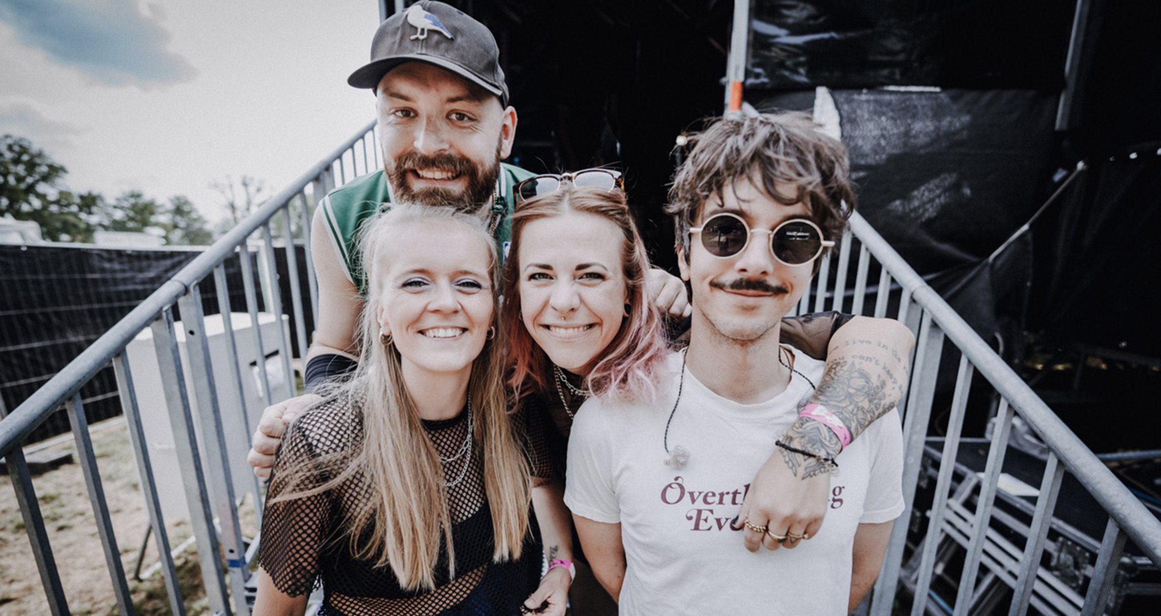 Vier Personen halten sich gegenseitig in den Armen und lachen breit in die Kamera.