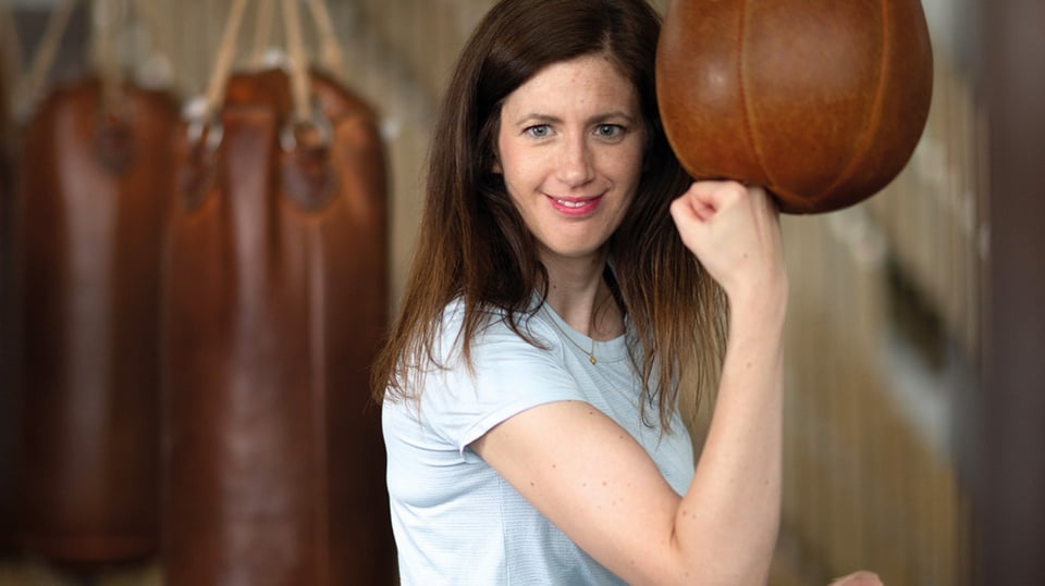 Claudia Pichler in weißem T-Shirt, die Hand zu einer Faust geballt, im Hintergrund Boxsäcke