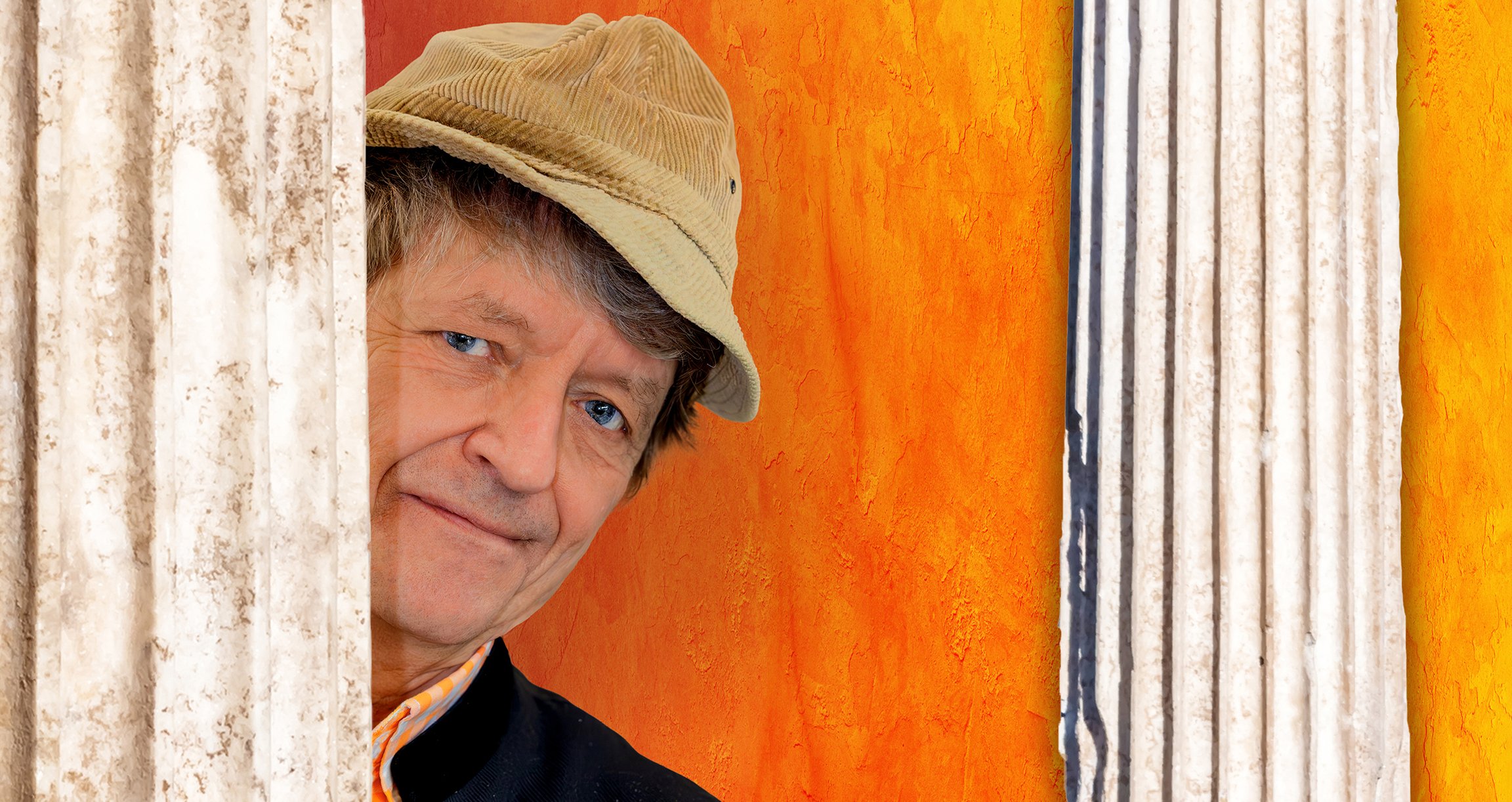 Foto von „Frank-Markus Barwasser“ mit orangefarbenem Hintergrund zwischen zwei Säulen