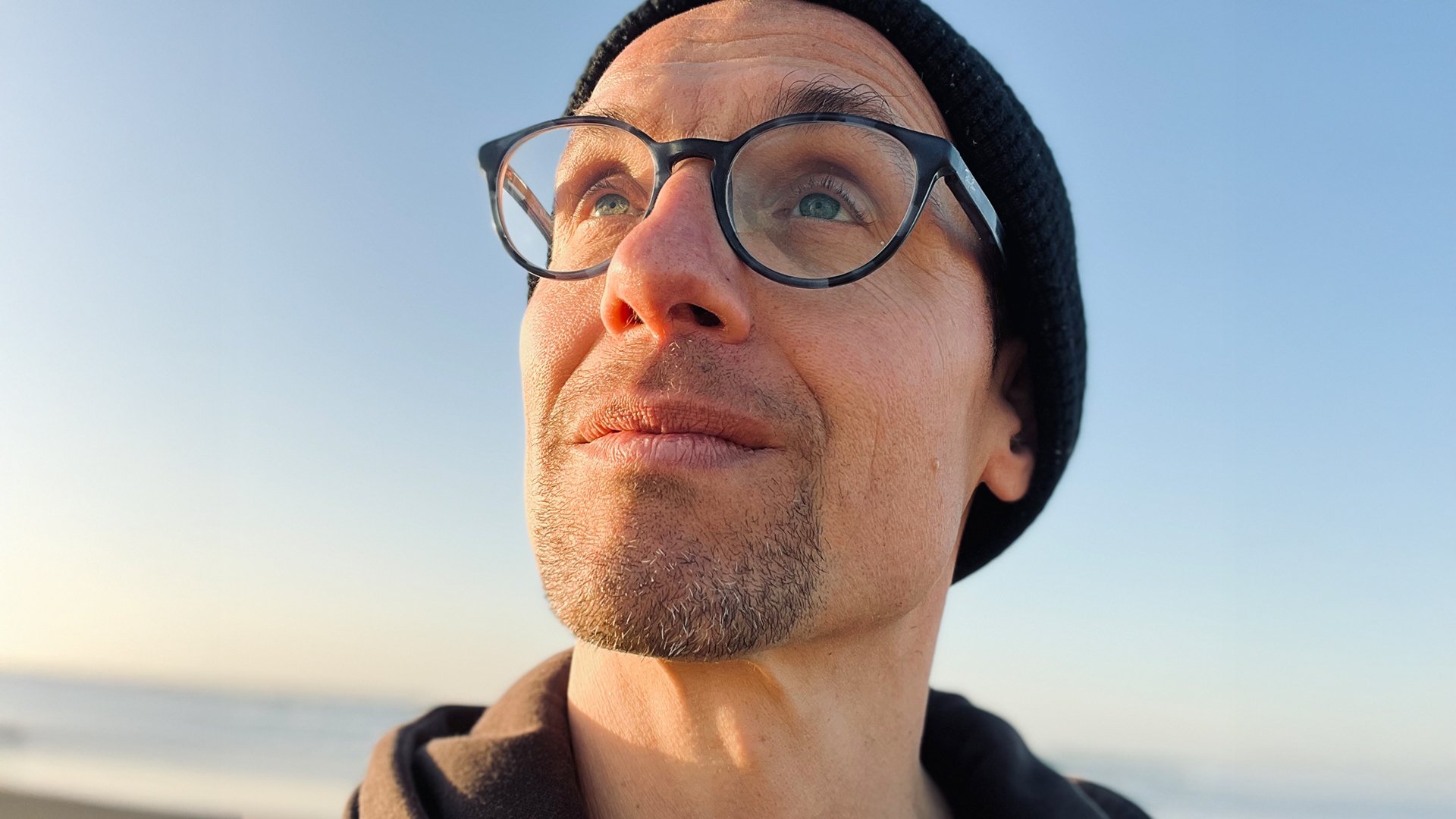 Frank Weigand mit Brille und schwarzer Mütze nach oben blickend vor blauem Himmel 