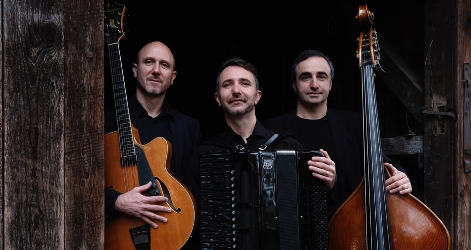 Drei Musiker vor dunklem Hintergrund mit Instrumenten in der Hand