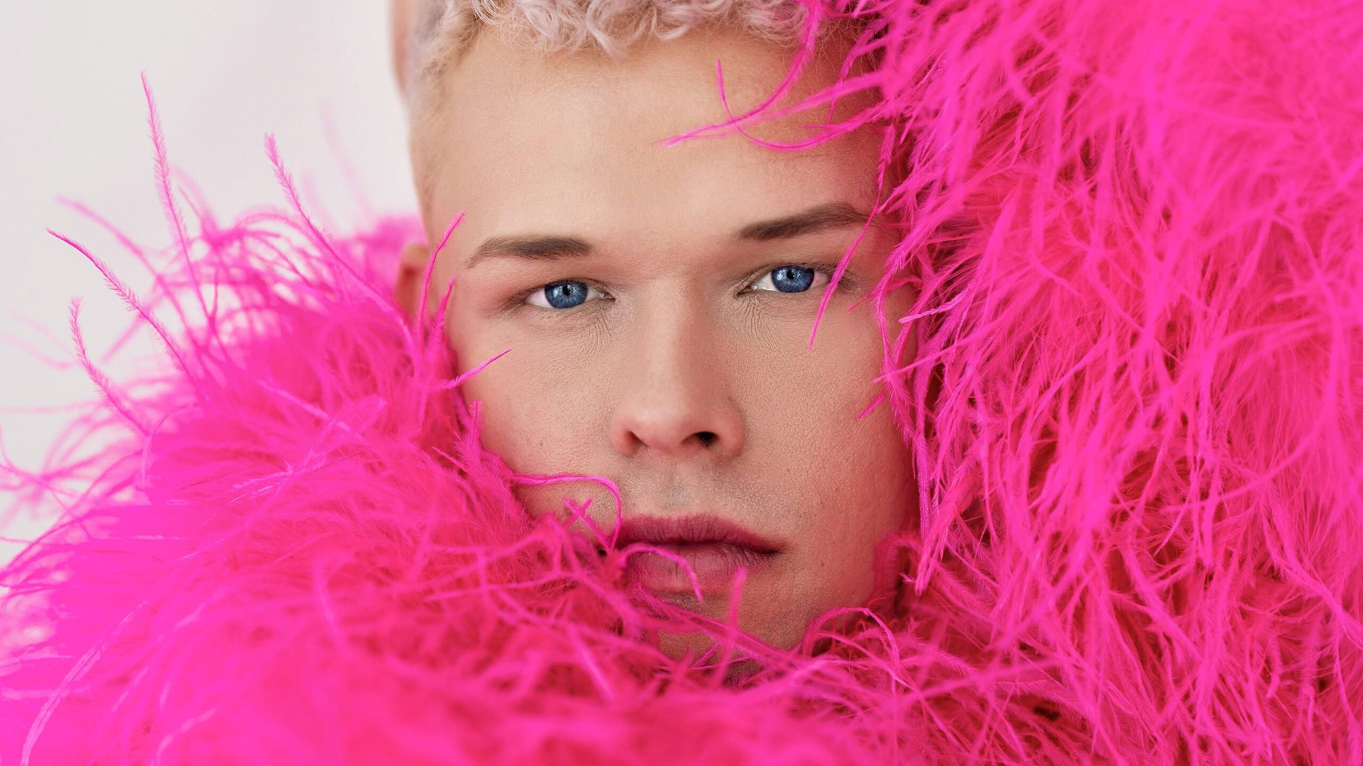 Foto für die Veranstaltung von Tobias Born mit dem Porträt des Künstlers, der eine Jacke aus langen, pink‑fuchsiafarbenen Fellfasern trägt