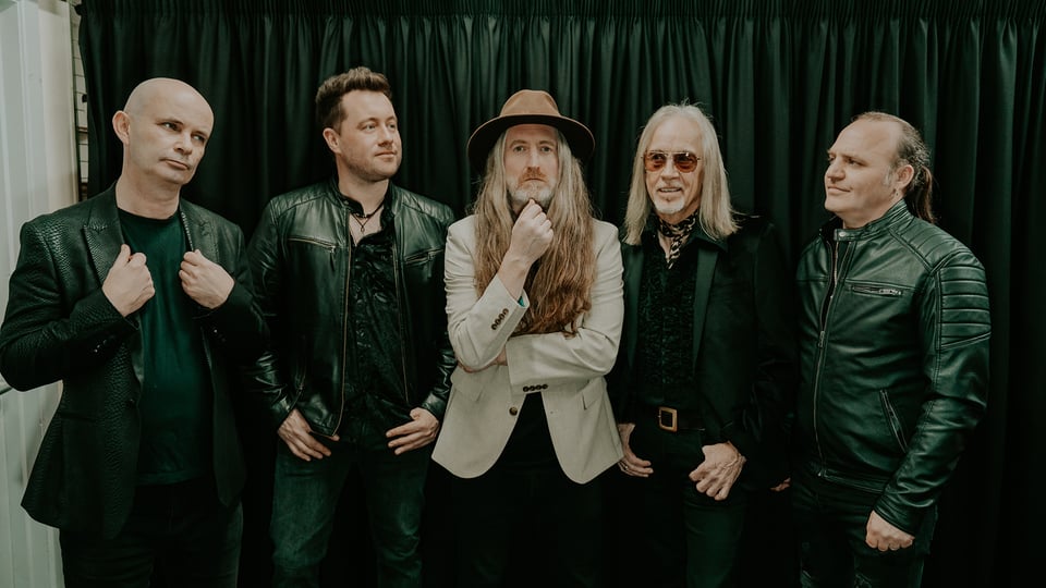 Die fünf Musiker der Band stehen vor einem dunkelgrünen Vorhang