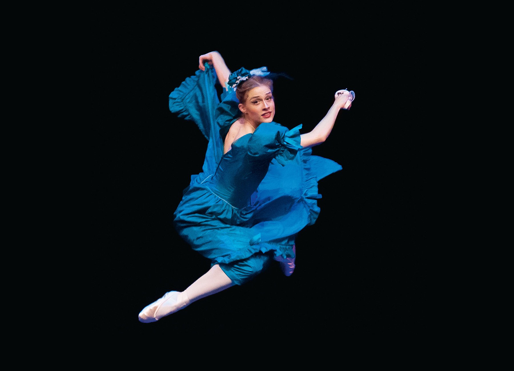Dame in blauem Kleid und Ballettschuhen, springend vor schwarzem Hintergrund