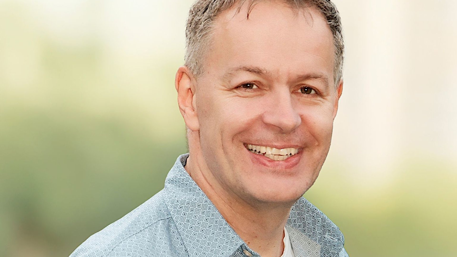 Ein Portrait von Steffen Möller in hellblau gemustertem Hemd vor hellgrün verschwommenen Hintergrund