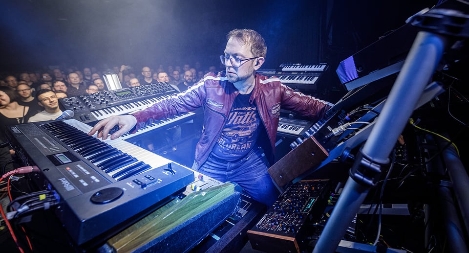 Auf dem Foto sieht man den Künstler bei einem elektronischen Konzert am Mischpult, umgeben vom feiernden Publikum