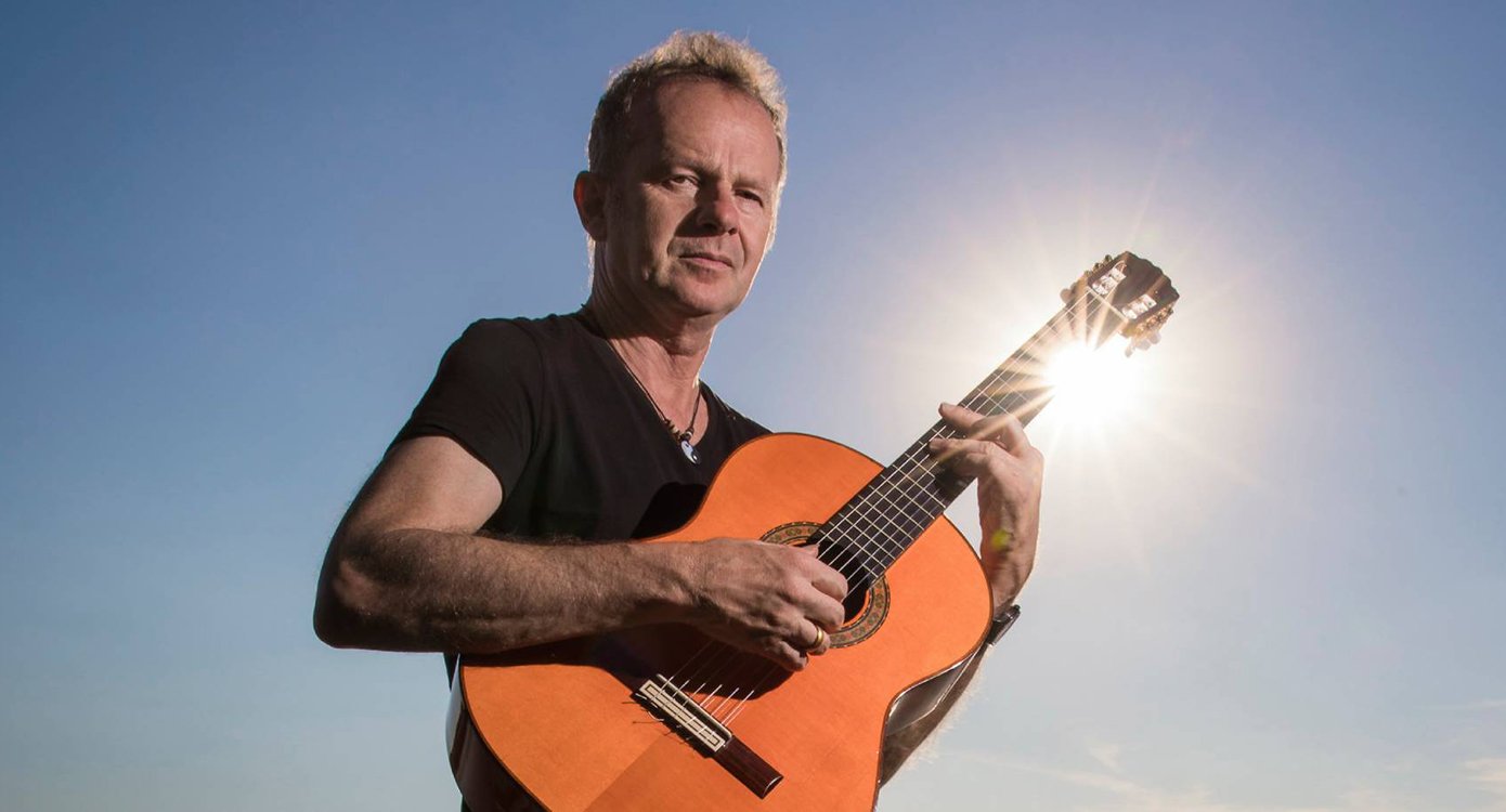 Foto eines Mannes mit Gitarre vor blauem Himmel