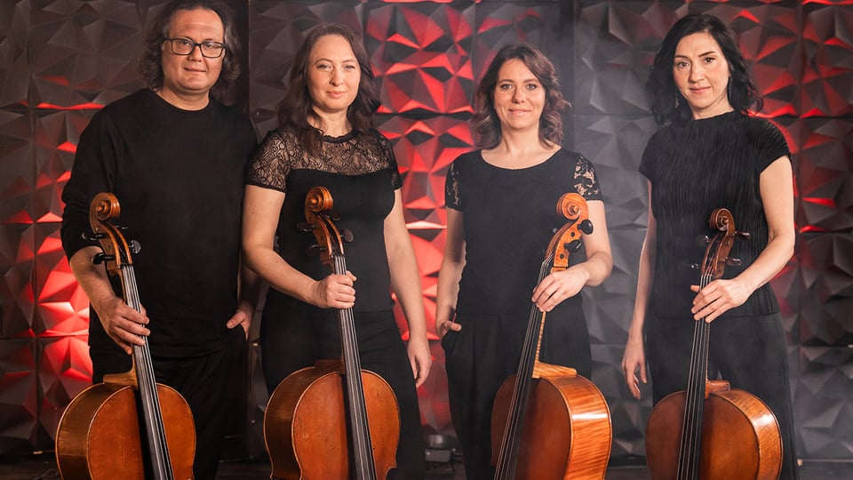 1 Mann und drei Frauen stehen schwarz gekleidet mit jeweils einem Cello in der Hand da