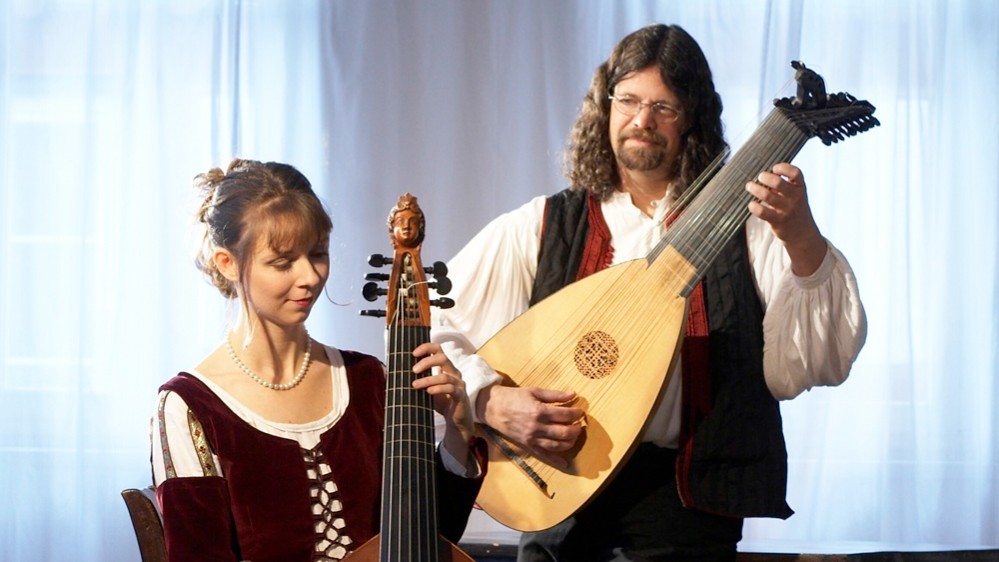Duo Kirchhof mit Viola da Gamba und Laute: Eine Musikerin im historischen Kleid sitzt mit Viola da Gamba und Bogen, ein Musiker steht daneben und spielt eine Laute, beide in historisch anmutender Kleidung vor hellem Vorhang.