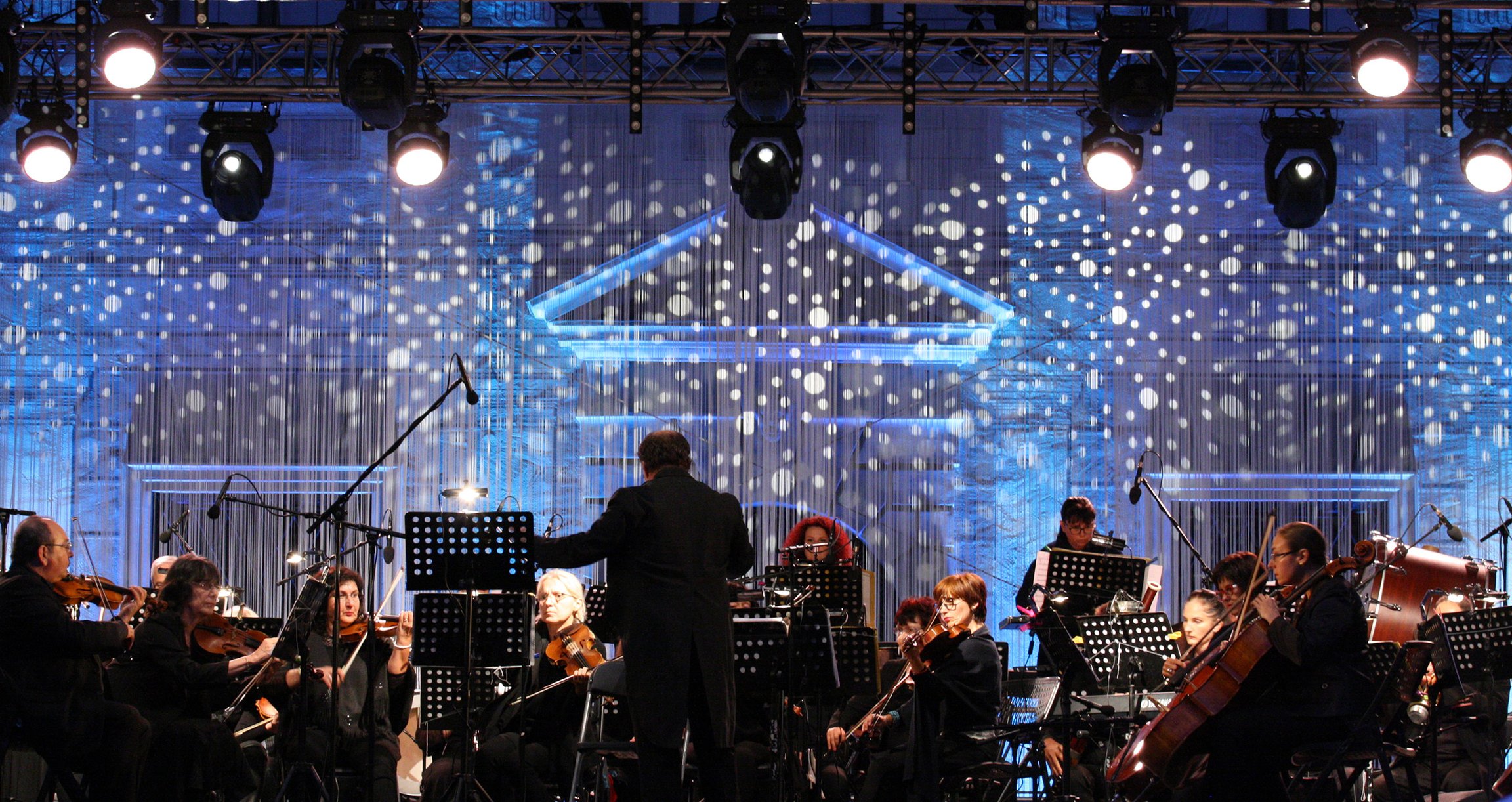 Orchester auf Bühne mit Dirigent in blauem Scheinwerferlicht