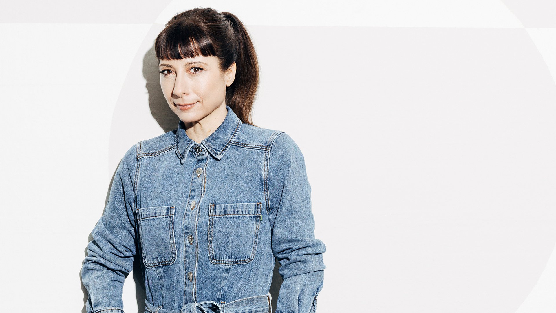 Porträt einer Person in Jeanshemd vor hellem Hintergrund, Studioaufnahme mit weichem Licht und minimalistischem Stil.