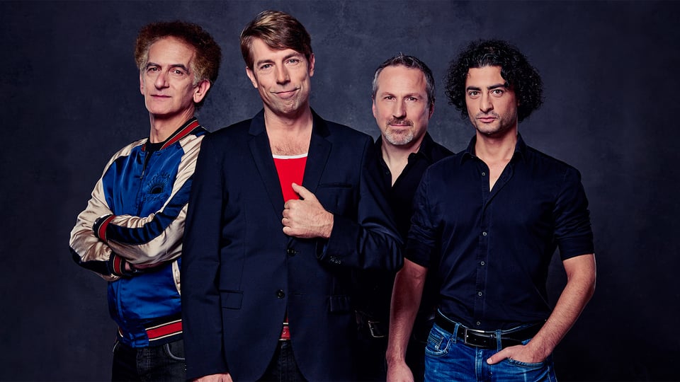 Die vier Musiker in blau-roter Kleidung vor dunkelblauem Hintergrund