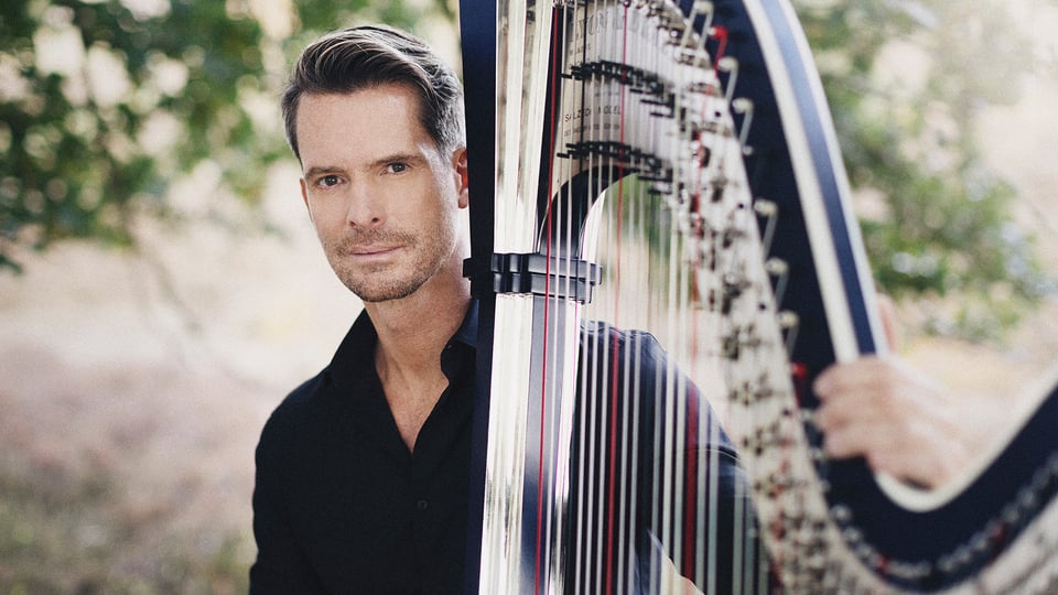 Promobild für das Event ‚Münchener Kammerorchester / Maistre‘: Eine Person in dunkler Kleidung steht im Freien neben einer großen Konzertharfe, deren Saiten und Rahmen im Vordergrund deutlich sichtbar sind. Im Hintergrund sind Bäume und unscharfe Natur zu erkennen