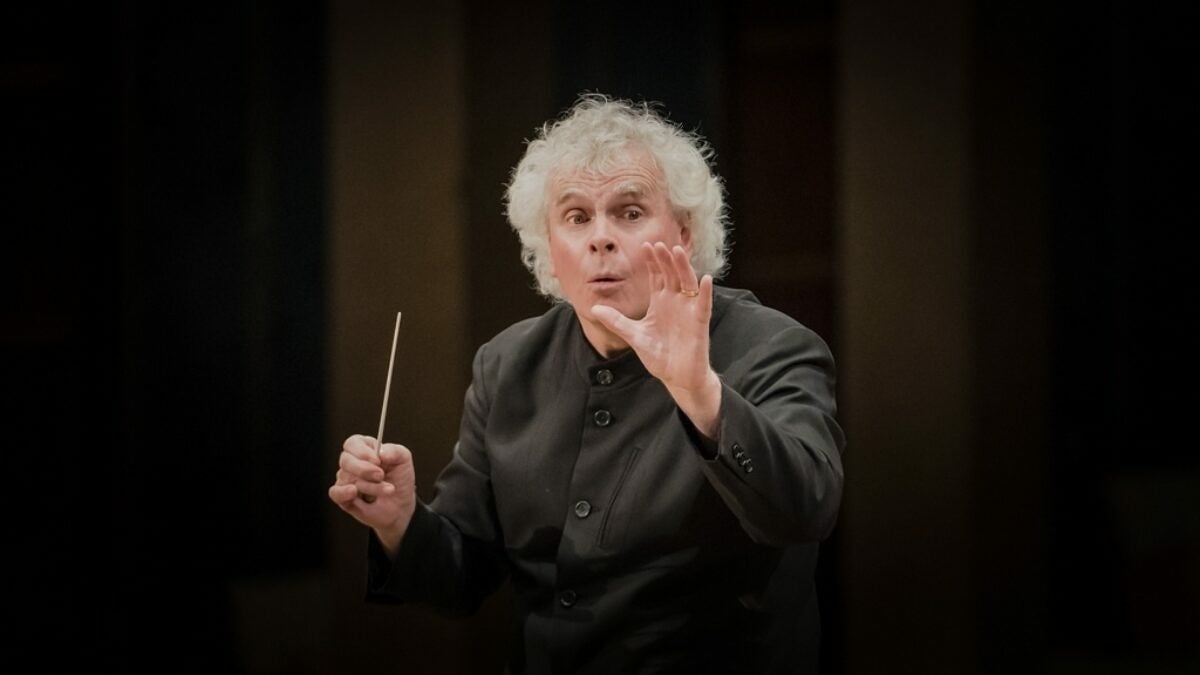 Sir Simon Rattle mit Dirigentenstock vor dunklem Hintergrund