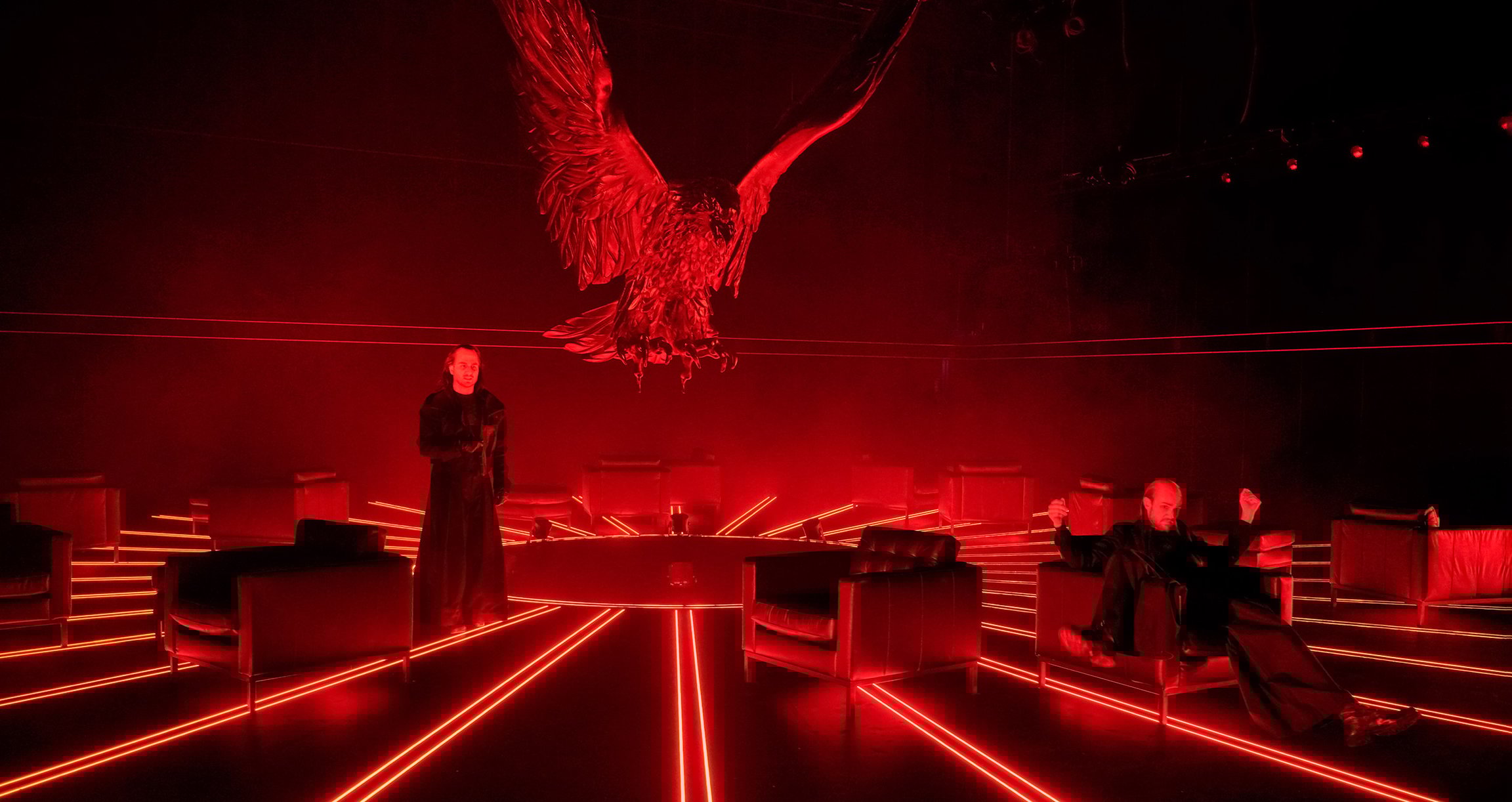 Foto von zwei Personen mit roten Lichtern und einem Adler darüber mit ausgebreiteten Flügeln.