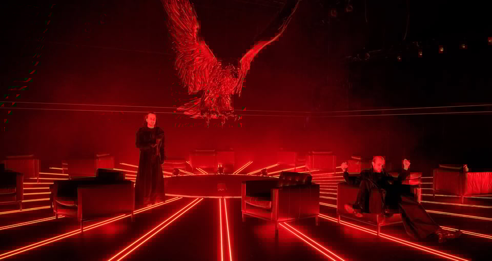 Foto von zwei Personen mit roten Lichtern und einem Adler darüber mit ausgebreiteten Flügeln.