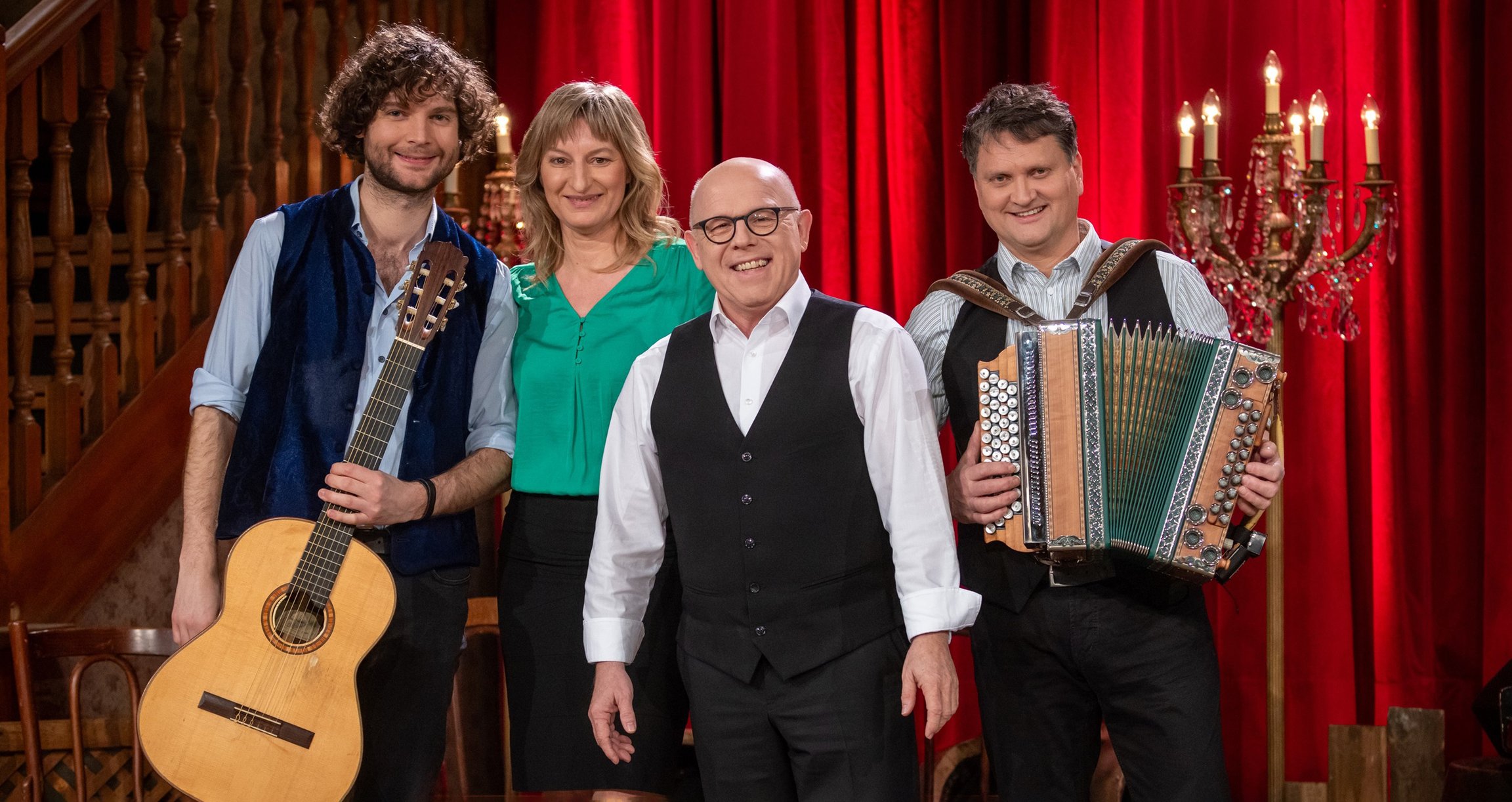 Foto von drei Männern und einem Mädchen mit Instrumenten und im Hintergrund eine Kulisse