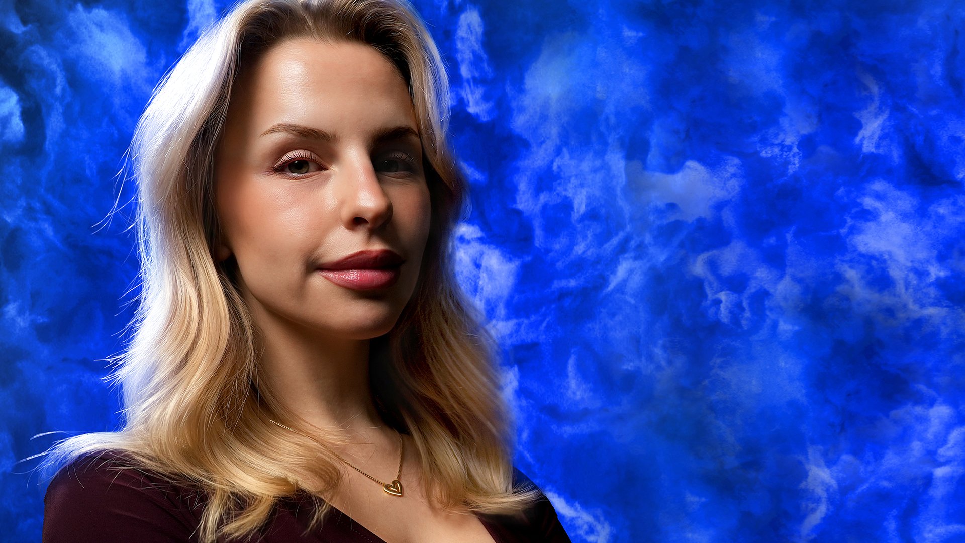 Porträt einer blonden Frau mit ruhigem Gesichtsausdruck vor blauem, wolkenartigem Hintergrund, aufgenommen als Bühnen- und Pressebild für die Show „Mord am Mittwoch – Die Crime Show 2027“ von Lucia Leona.