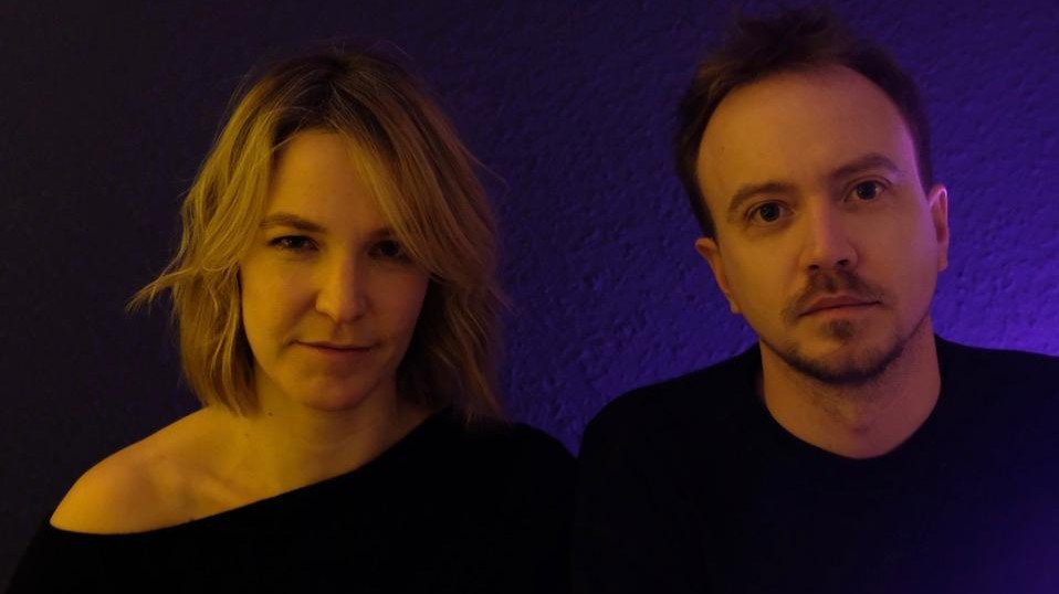 Pressefoto des Duos Melisa & Uli, Porträtaufnahme vor dunklem Hintergrund mit farbiger Beleuchtung.