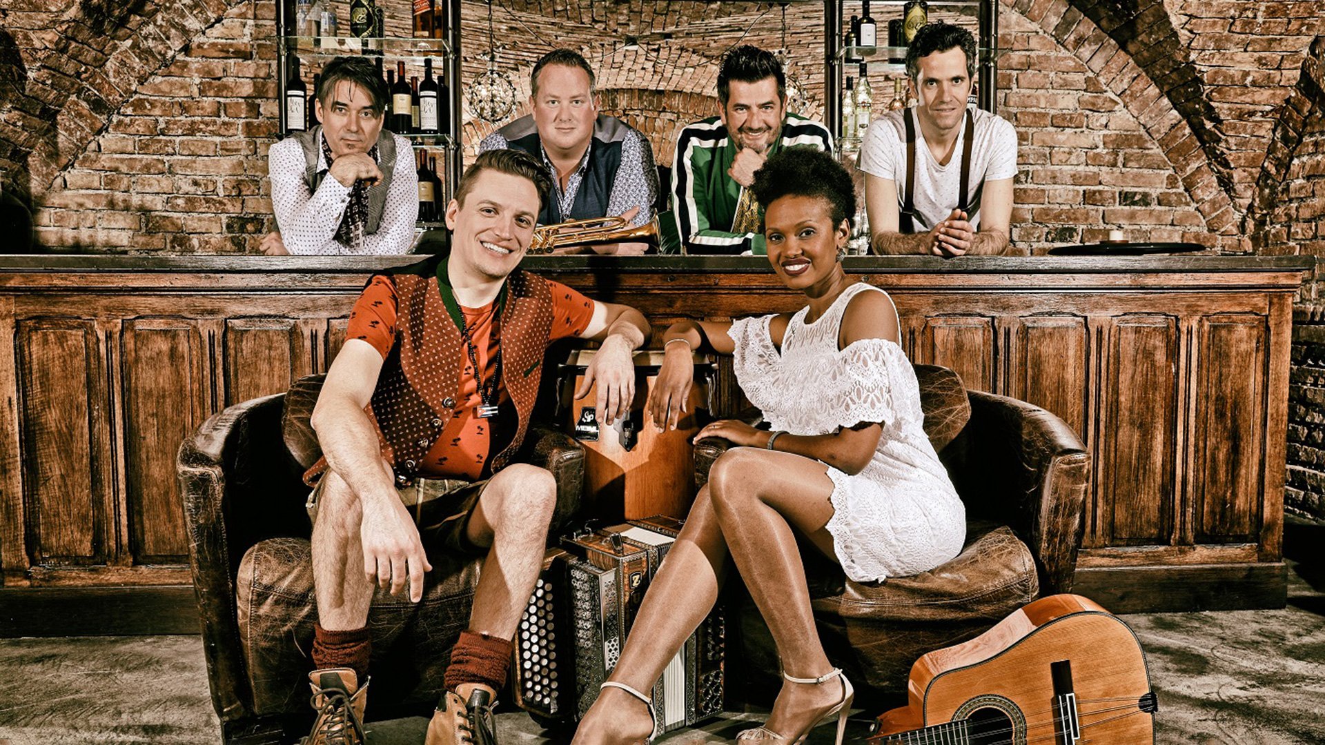 Foto von der Veranstaltung Cubaboarisch 2.0 - Havanna Viva! mit den Künstlern hinter einer Bar und zwei anderen, die auf einem Sofa sitzen