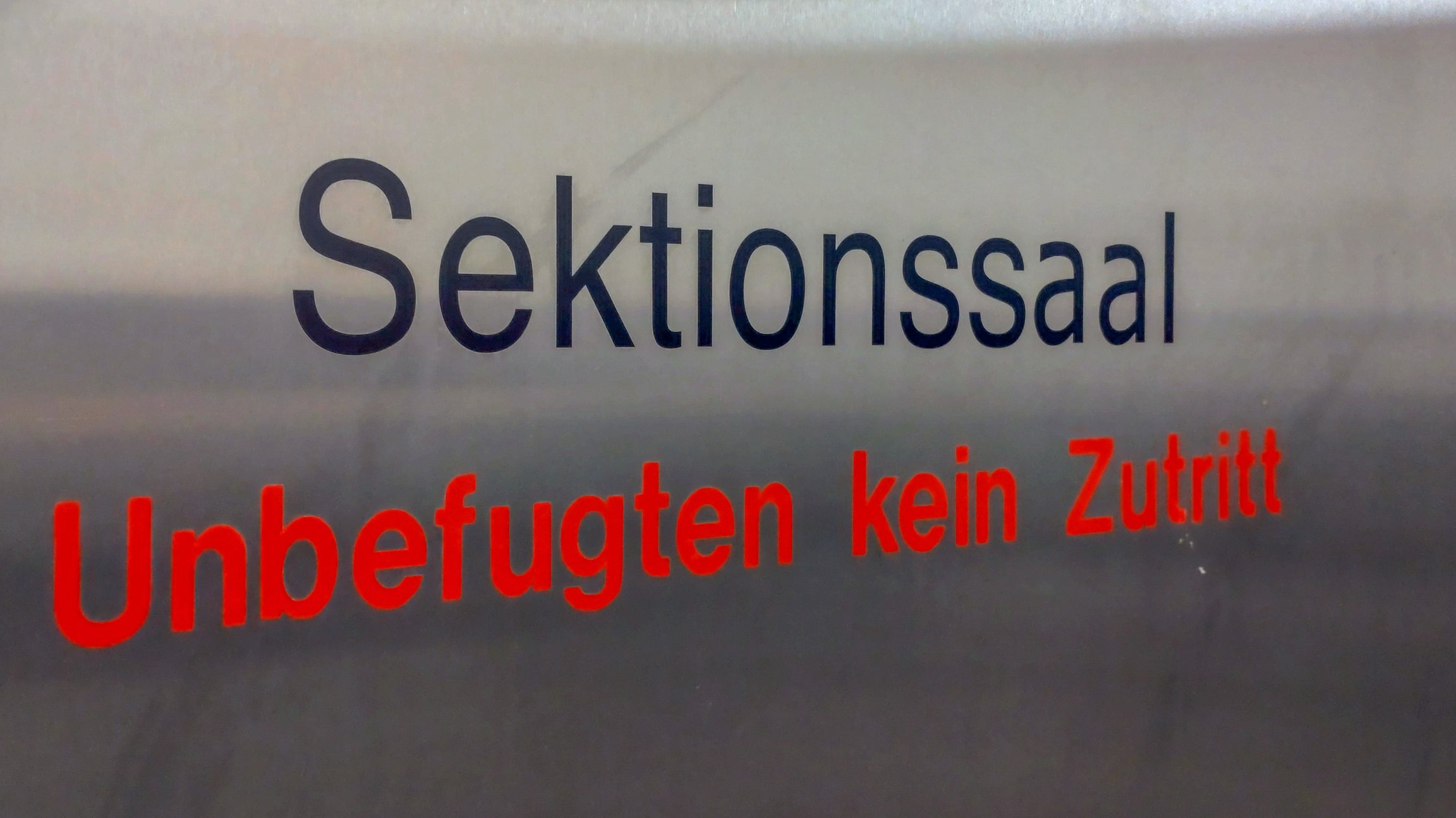 Ein Schild mit der Aufschrift Sektionssaal in schwarz und Unbefugten kein Zutritt in rot