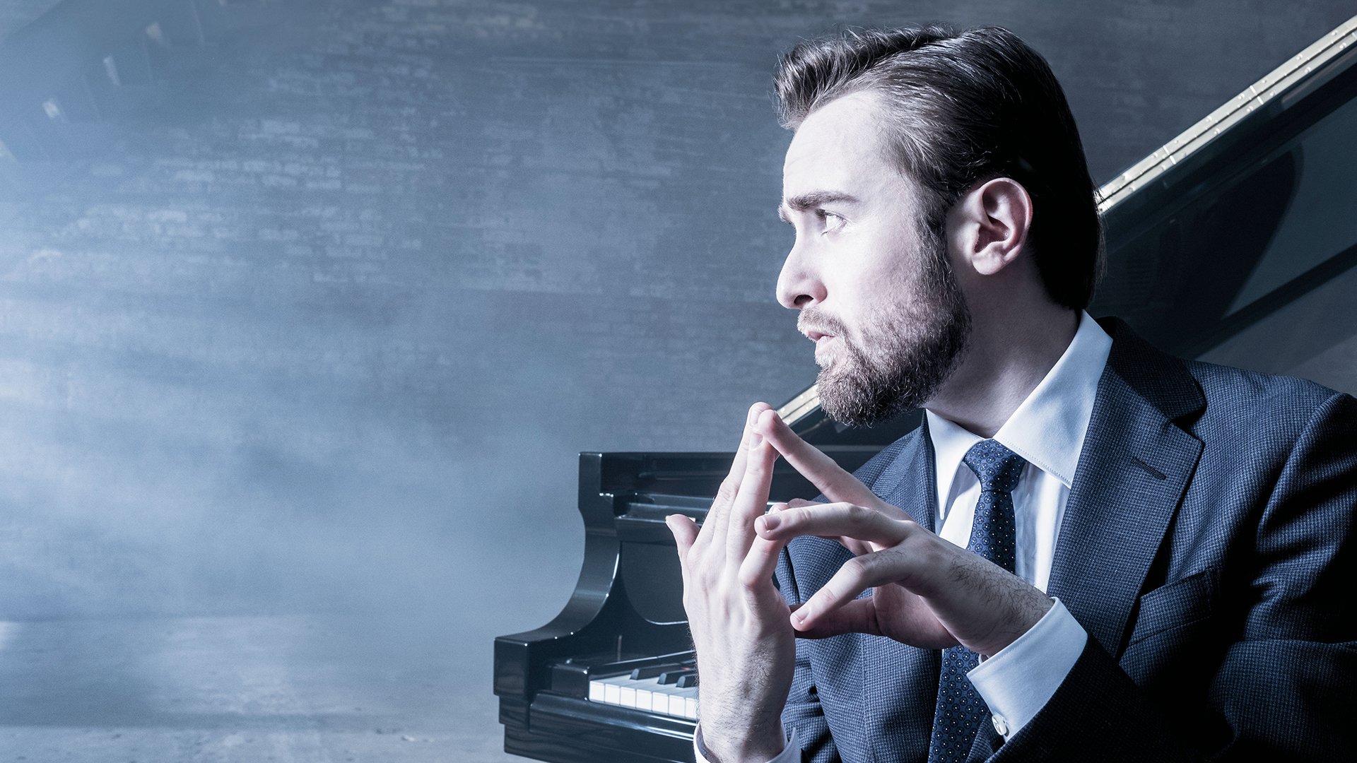 Promobild für das Event ‚Daniil Trifonov & Berliner Barocksolisten‘: Eine Person im dunklen Anzug sitzt vor einem Flügel in einem neblig beleuchteten Raum und hält die Hände vor dem Instrument