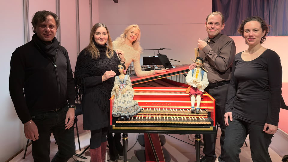 Fünf Personen stehen neben einer roten Orgel, zwei Personen halten Marionetten in den Händen