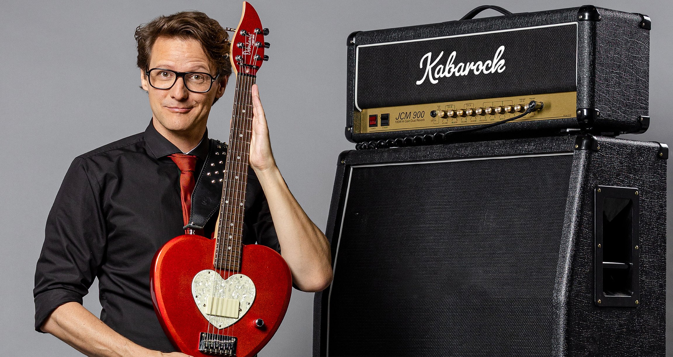 Foto der Veranstaltung Bewie Bauer: EIN TEENAGER WIRD 50 mit einer roten Gitarre und einem schwarzen Lautsprecher.