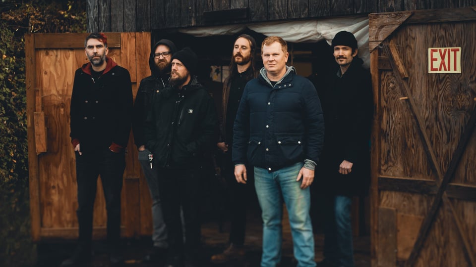 Die Band vor einer Holzhütte stehend