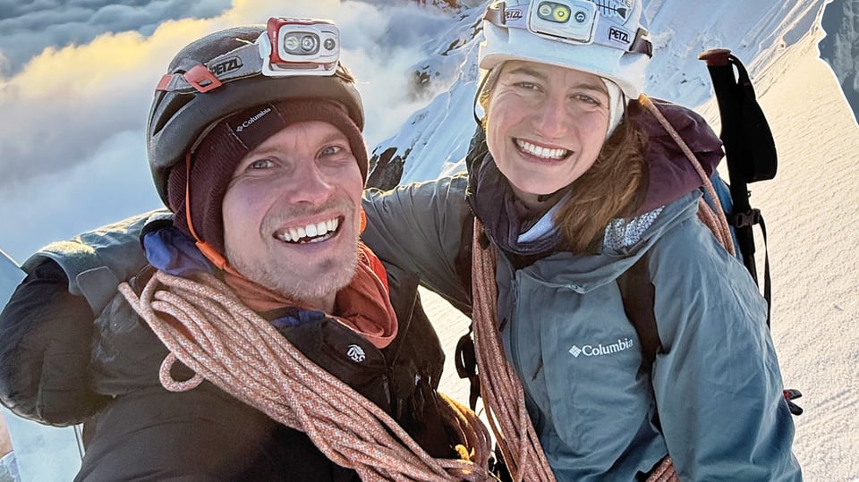 Lukas Irmler und Antonia Rüede-Passul mit Ausrüstung lachend vor Bergkulisse