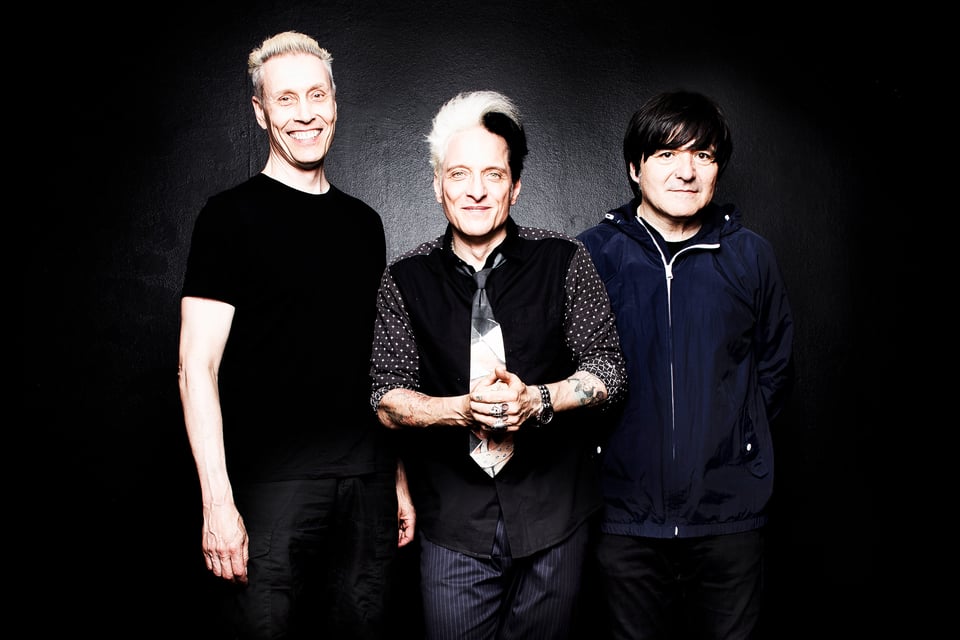 Die Ärzte gucken frontal in die Kamera und stehen vor einer dunklen Wand.