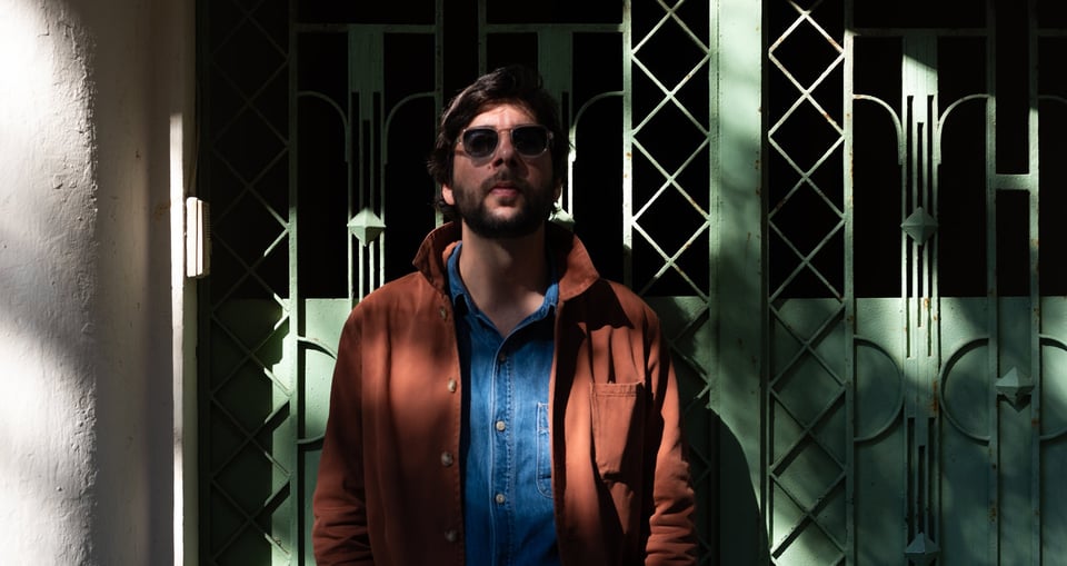 Mann in brauner Jacke mit blauem Hmd und Sonnenbrille vor Eisentor